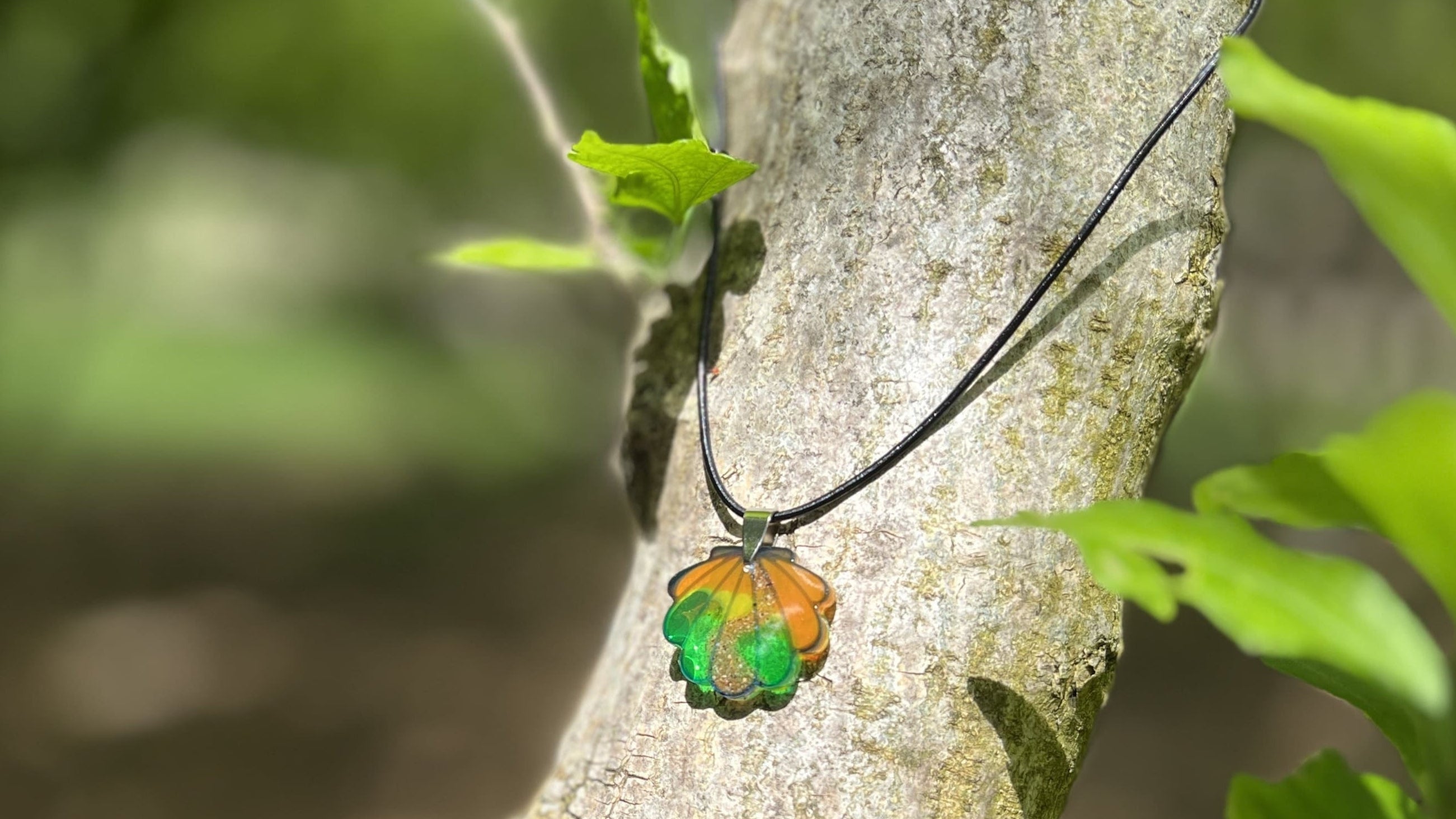 Collar con concha del Camino de Santiago hecho a mano, colocado sobre una hoja en el césped. Un recuerdo artesanal, único y lleno de significado.