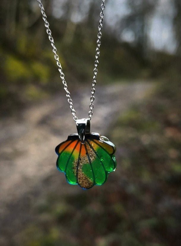 El mejor regalo del camino de Santiago para peregrinos que vivieron el camino de verdad. 
Concha atardecer colgada en un árbol, con el Camino de Santiago desenfocado al fondo. Un collar artesanal que representa el viaje y sus recuerdos más profundos.